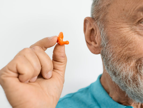 Older man holding a custom-molded earplug near his ear
